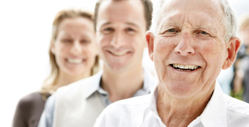 An older gentleman, a young man and a woman stood in a line smiling